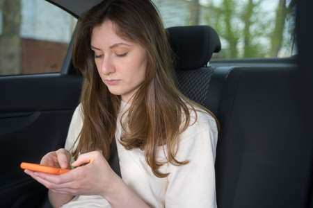 Female passenger in the car looks and types in the phone. Social Media in transportation
