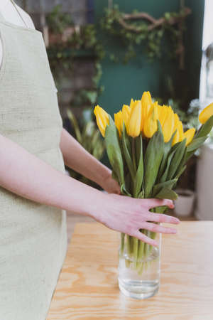 A feminine florist puts a bouquet of beautiful flowers in a transparent glass vaseの写真素材