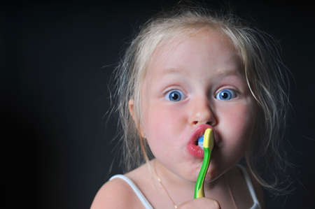 little girl brushing her teeth, girl brushing her teeth, funny little girl brushing her teeth, dark backgroundの写真素材