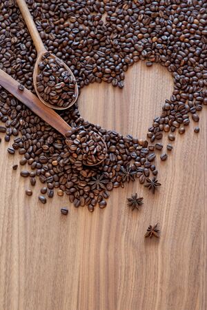 Coffee beans spilled on a heart-shaped wooden table with spices with two wooden spoons. Great background for cafe menu design.の写真素材