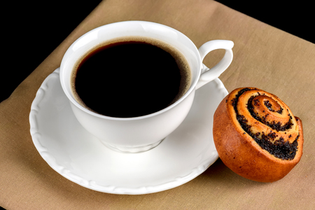 A cup of coffee a bun with poppy seeds on a black backgroundの写真素材