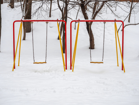 Multicolored snow-covered swing for children in the park in winter.の写真素材