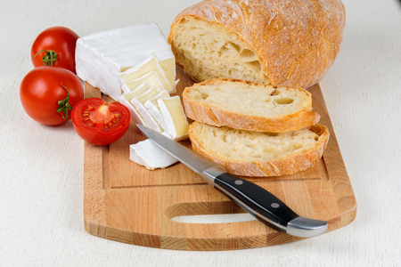 Cheese, tomatoes and bread sliced for breakfast on a wooden board.の写真素材