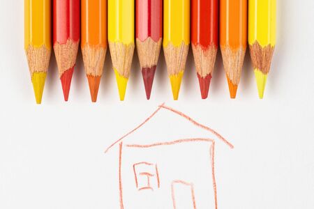 Colored pencils on a white sheet of paper on which the house is painted. Pencils red and yellow on a white background.の写真素材
