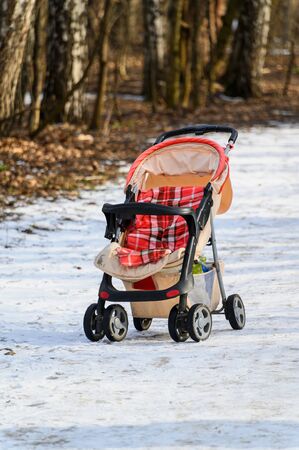 An empty baby stroller on the path in the winter Park.