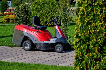 A red self-driving lawn mower stands without a driver in the Park. Mowing grass in the Park with a...