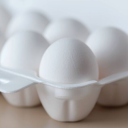 White raw chicken eggs in a plastic tray close-up. Chicken eggs background.