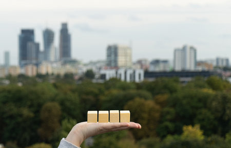 Hand holding blank wooden blocks on blurred city background. Wooden cubes mockup, empty wooden blocks with copy space, wood cubes for new year business text, calendar conceptの写真素材