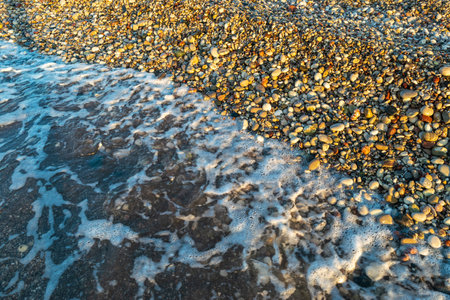 Sea waves on pebble beach texture background. Transparent ocean water, rocky shore pattern, summer mockup with copy space, stone shoreline, vacation conceptの写真素材