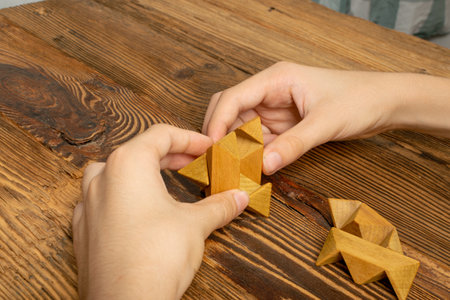 Wood puzzle pieces in kid hands, brain teaser. Wooden game block, brainteaser logic game, mechanical...
