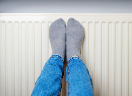 Warming Feet on White Radiator, Man Warms his Feet at Home, Cold Winter, Expensive Electricity Saving Concept, Copy Spaceの写真素材