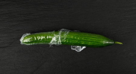 Plastic Wrapped Cucumber, Vegetable in Film Packaging, Film Wrap Food, Eat Plastic Concept, Black Backgroundの写真素材