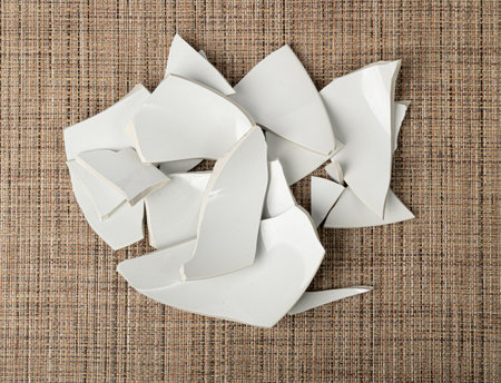 Broken Plate on Table, White Ceramic Pieces, Smashed Crockery Bowl, Stress Concept, Porcelain Shards on Brown Backgroundの写真素材