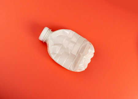 Empty Plastic Milk Bottle, Crumpled White Plastic Bottle, Global Pollution Concept, Squashed Pet Bottles on Red Backgroundの写真素材