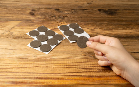 Adhesive Felt Pads Floor Protectors, Anti-Skid Felt Stickers for Chair Legs, Hand Holds Anti-Noise Coating, Furniture Floor Care, Wooden Backgroundの写真素材