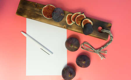 work table with blank sheets and pen, sliced fresh juicy figs, pink background. Planning concept,...