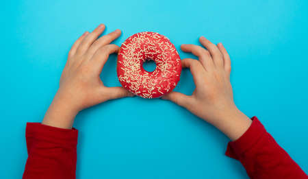 The perfect concept for food creation. Photo of a delicious donut with colorful splashes and two baby hands. Isolated on pastel blue backgroundの写真素材