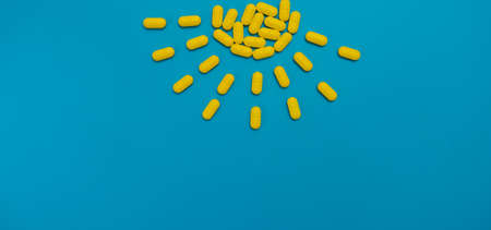 Yellow vitamins medicine capsules pills isolated on blue background. Health concept, drugs and danger.の写真素材