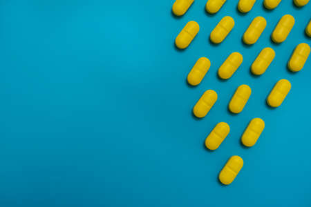 Yellow vitamins medicine capsules pills isolated on blue background. Health concept, drugs and danger.の写真素材