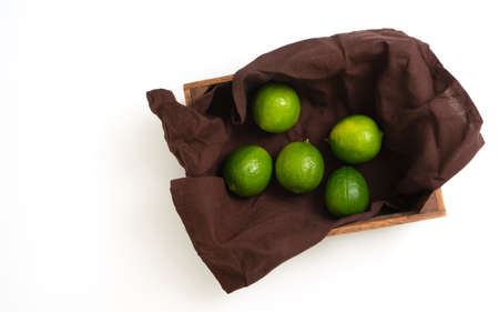 Limes in a wooden box on a napkin with copy space. Top view of fresh citrus fruits on white checkered napkin. Isolate.の写真素材