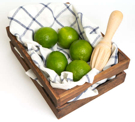 Limes in a wooden box on a napkin with copy space. Top view of fresh citrus fruits on white checkered napkin. Isolate.の写真素材