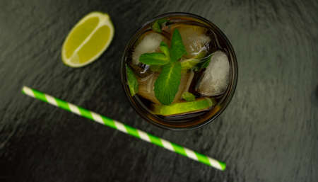 Cuba Libre cocktail with brown rum, lemon juice, cola and ice cubes, garnished with a slice of fresh lime on a modern black stone tray. Bar conceptの写真素材