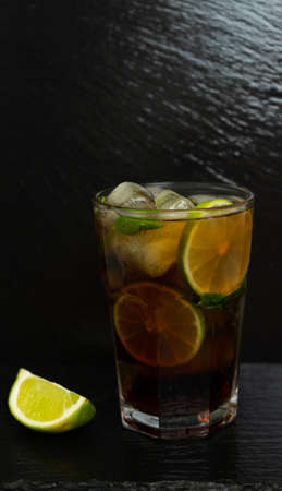 Cuba Libre cocktail with brown rum, lemon juice, cola and ice cubes, garnished with a slice of fresh lime on a modern black stone tray. Bar conceptの写真素材