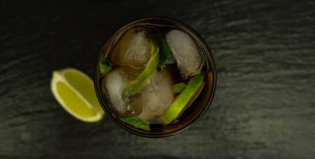 Cuba Libre cocktail with brown rum, lemon juice, cola and ice cubes, garnished with a slice of fresh lime on a modern black stone tray. Bar conceptの写真素材