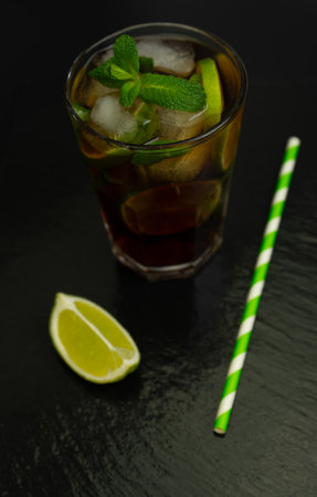 Cuba Libre cocktail with brown rum, lemon juice, cola and ice cubes, garnished with a slice of fresh lime on a modern black stone tray. Bar conceptの写真素材
