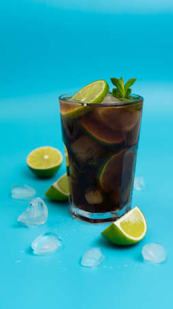 summer cooling cocktail with rum, ice and ripe lime sliced into wedges on a clean blue backgroundの写真素材