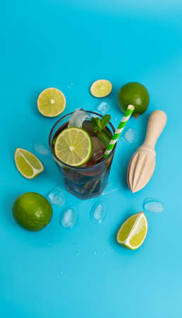summer cooling cocktail with rum, ice and ripe lime sliced into wedges on a clean blue backgroundの写真素材