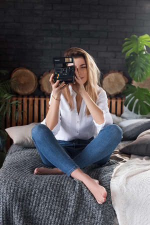 Moscow, Russia, 23 Mar 2019. Pretty girl sitting on a couch in a room covering face with polaroid camera having funのeditorial素材