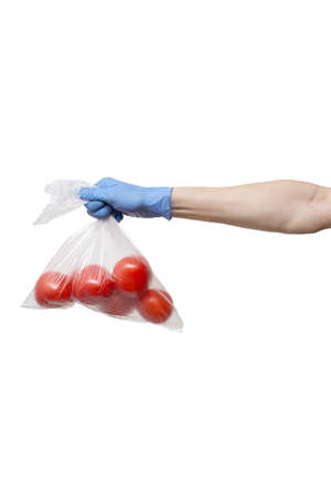 polythene bag of tomatoes held in hand wearing blue gloves on white backgroundの写真素材