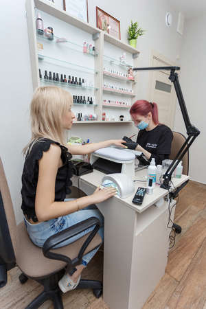 Russia, Moscow, 18 May 2019. Nail master wearing mask and black gloves making nails to a smiling pretty girl with brushのeditorial素材