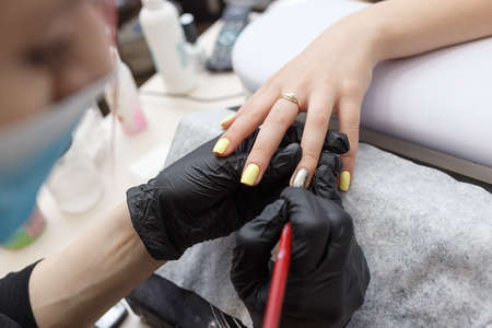 Nail master wearing a mask and black gloves applying brush on acrylic nails in the salon. Closeupの写真素材