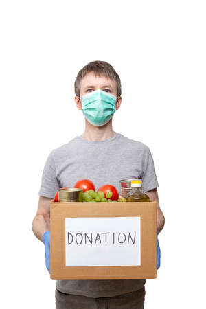 volunteer in blue protective gloves holding grocery food in carton donation boxの写真素材