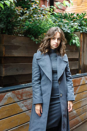 portrait of young thoughtful girl in gray coat and turtleneck posing outdoorsの写真素材