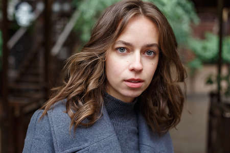portrait of young thoughtful girl in gray coat and turtleneck posing outdoorsの写真素材