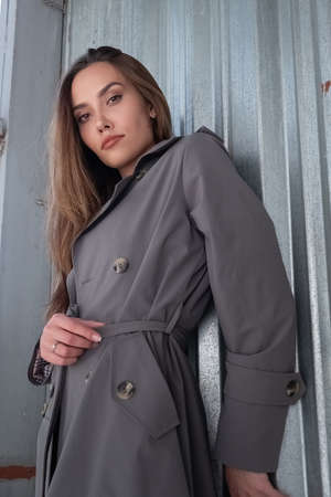 attractive young asian model in gray trench coat standing near wall outdoors