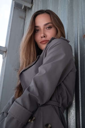 attractive young asian model in gray trench coat standing near wall outdoorsの写真素材