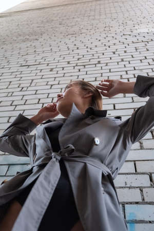 attractive asian model in trench coat standing near wall shot from lower pointの写真素材