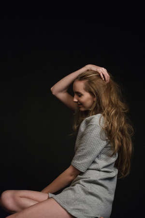 young pretty woman with long hair in dress sits and smiles on black backgroundの写真素材