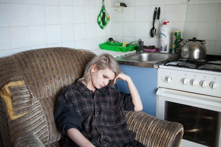 young attractive female with short hair sitting in dilapidated armchair at old vintage kitchen