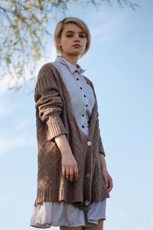 young attractive caucasian female with short hair in spotted dress and sweater standing in front of...