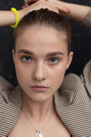 closeup portrait of young attractive caucasian woman with blue eyes in suit jacket. skinny pretty lady posing in front of studio flag, collecting her hair in ponytail. model tests of beautiful ladyの写真素材