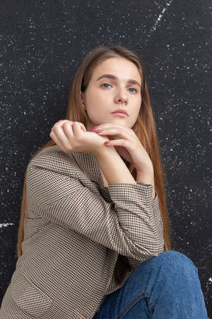 portrait of young attractive caucasian woman with long hair, blue eyes in suit jacket. skinny pretty lady sitting and posing in front of studio flag. model tests of beautiful ladyの写真素材