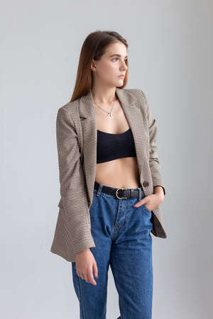 portrait of young attractive caucasian woman with long brown hair in suit jacket and blue jeans. skinny pretty lady posing on white or grey background at studio. model tests of beautiful ladyの写真素材