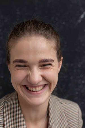 closeup portrait of young attractive caucasian smiling woman with brown hair in suit jacket. skinny happy pretty lady posing in front of studio flag. model tests of beautiful ladyの写真素材