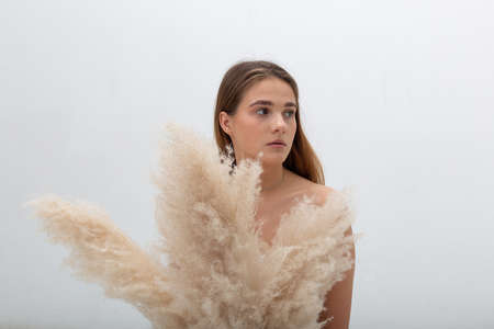 portrait of young caucasian woman with long hair holding bouquet of pampas grass on white...