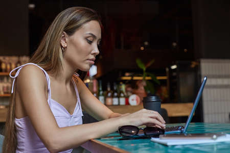 beautiful young asian woman sitting at table of coffee shop, working on laptop. attractive student lady studying at cafe, doing homework. modern online education, distant work, remote job, freelanceの写真素材